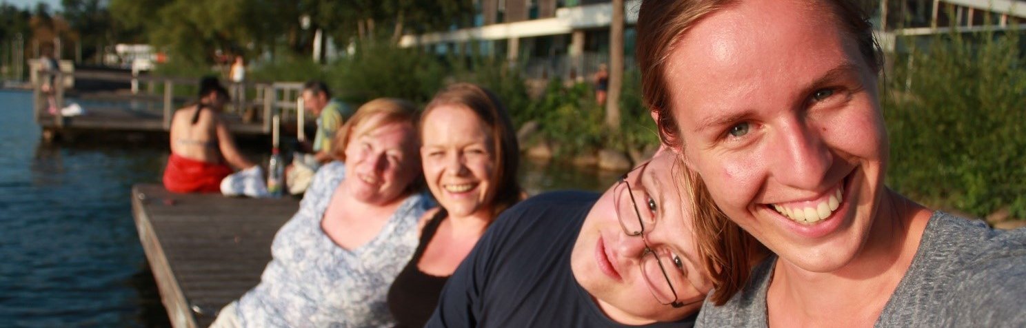 Vier Menschen sitzen an einem Bootssteg und lächeln in die Kamera.