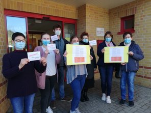 Auf dem Bild zeigen sieben Mitarbeiter:innen der Kita Schatzinsel die Plakate und Postkarten für den Protest.