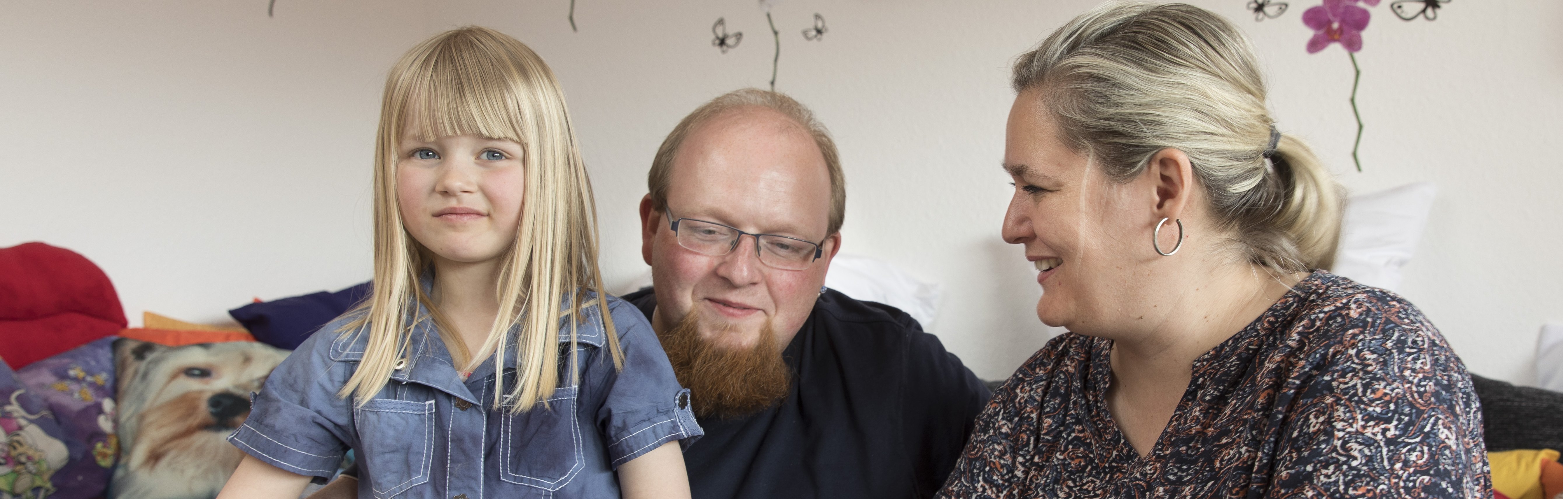 Ein Vater hat seine Tochter auf dem Schoss. Eine Mitarbeiterin berät die beiden.