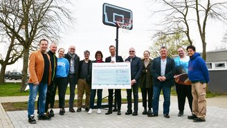 12 Personen stehen vor dem neuen Basketballkorb. In der Mitte wir ein großer Schauscheck gehalten.