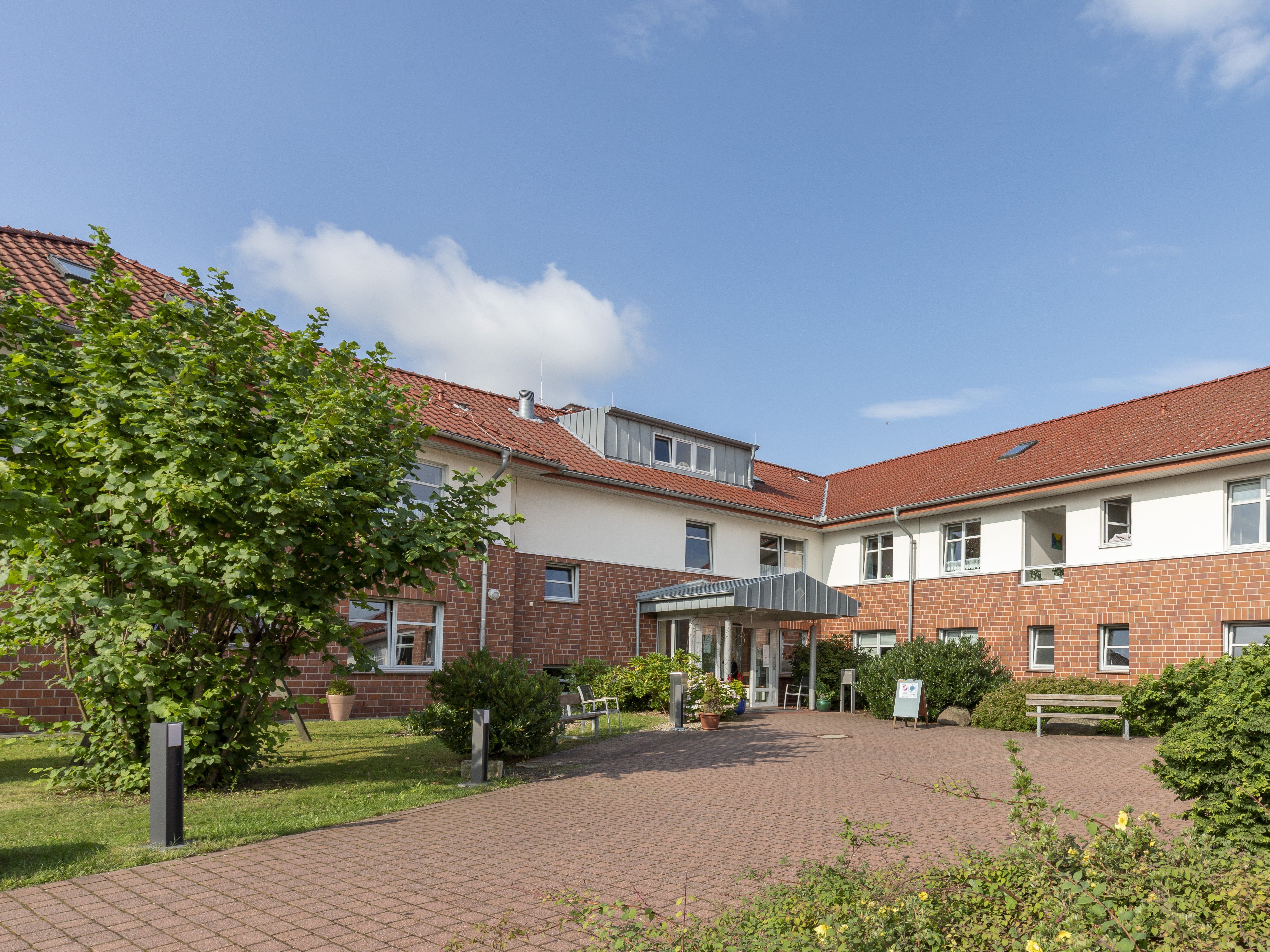 Das zweigeschossige Haus ist unten aus rotem Backstein und oben weiß. Vor dem Haus ist eine große Auffahrt. 