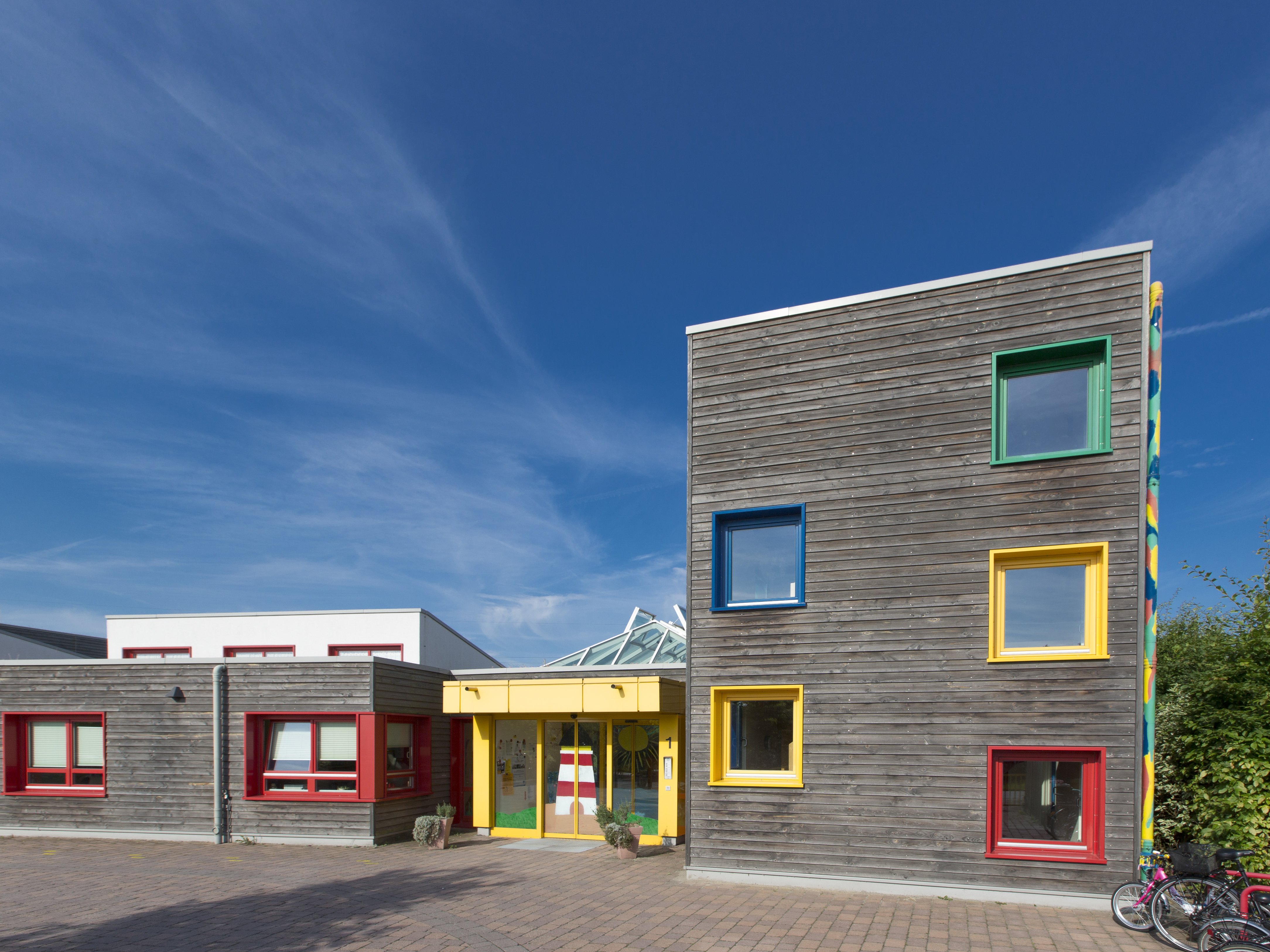 Das Haus der Kita Vin hat eine Fassade aus Holz. Die Fensterrahmen und der Eingang sind farbig. 