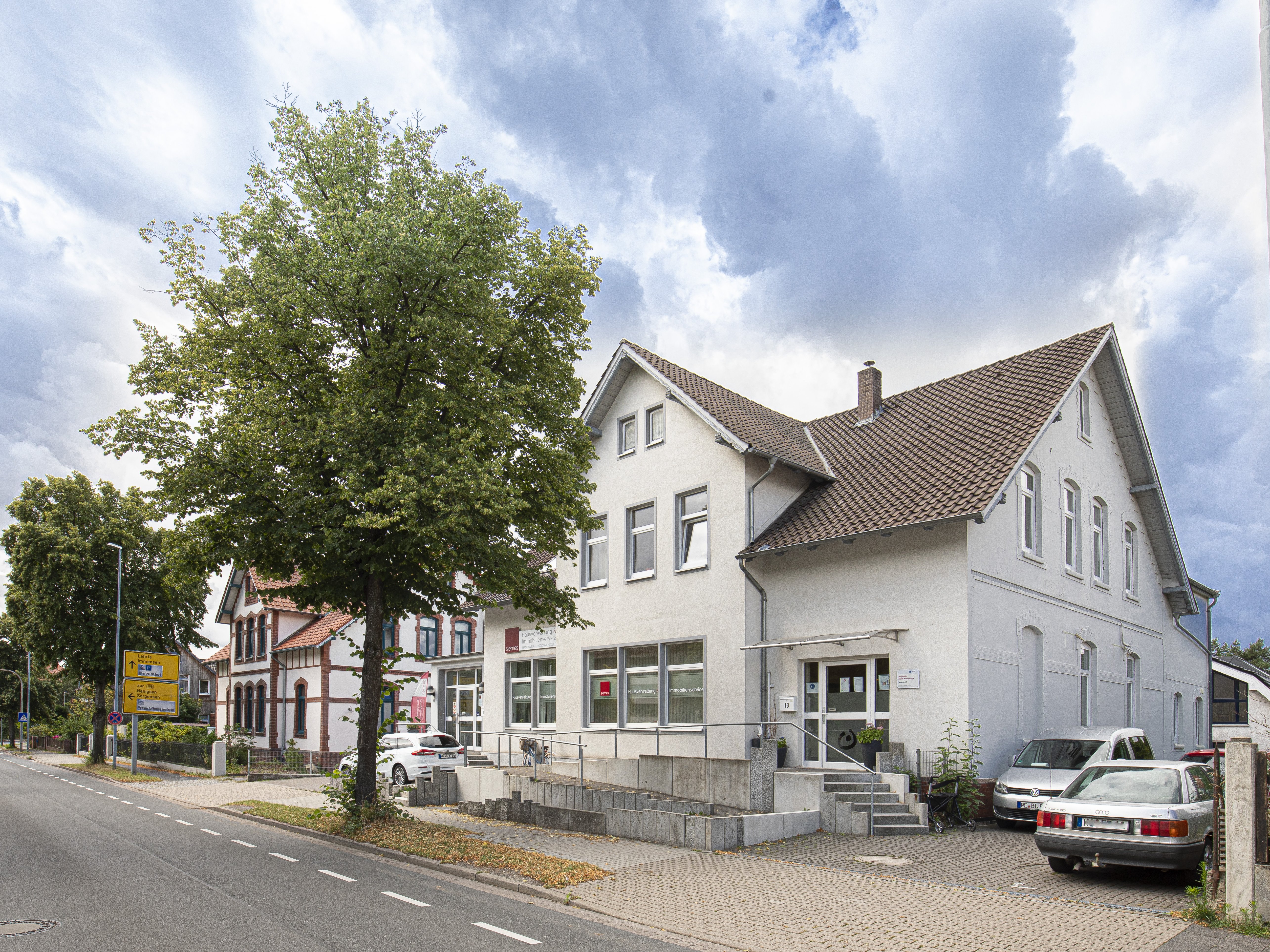 Ein weißes, zweigeschossiges Haus direkt an der Straße, mit kleiner Auffahrt.