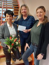 Drei Personen stehen auf einer Treppe. Von links nach rechts sind es: Petra Franke mit einem Blumenstrauß, Birgit Graumann mit einem Umschlag in dem die Spende ist und Michaela Kantak.